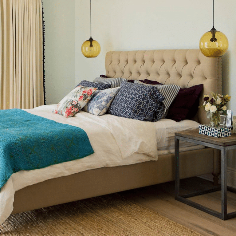 Bedroom with a beige tufted headboard, white bedding, turquoise throw, and patterned pillows on the bed.