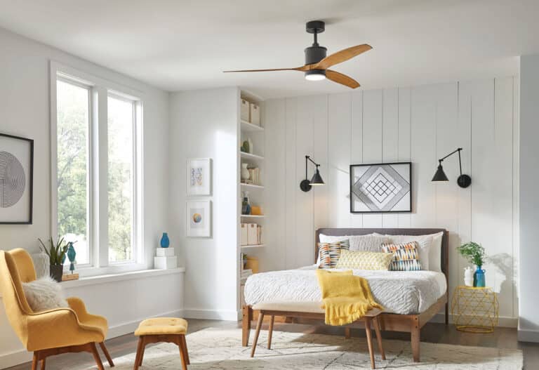 Bright modern bedroom with white paneled walls, wooden bed, and yellow accent throws; large windows reveal greenery outside.