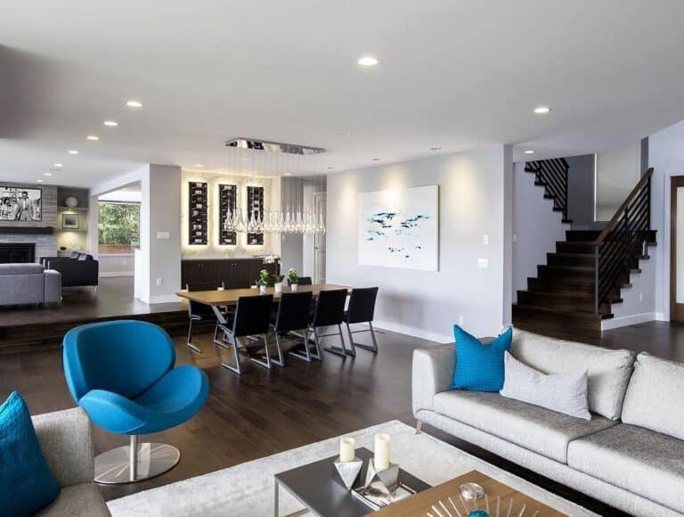 Open-concept living and dining room with dark wood floors, gray sofas, blue throw pillows, and a blue accent chair.