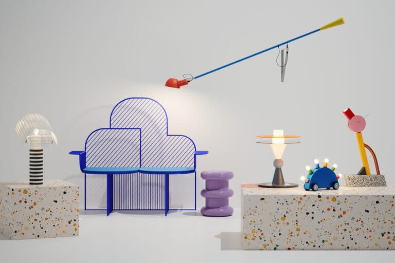 Studio scene with a blue striped metal chair, purple stacked stools, terrazzo blocks, and whimsical lamps and toys on display.