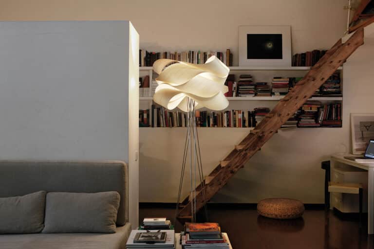 Cozy living room with a sculptural white floor lamp, wooden ladder to shelves full of books, and a gray sofa with cushions.