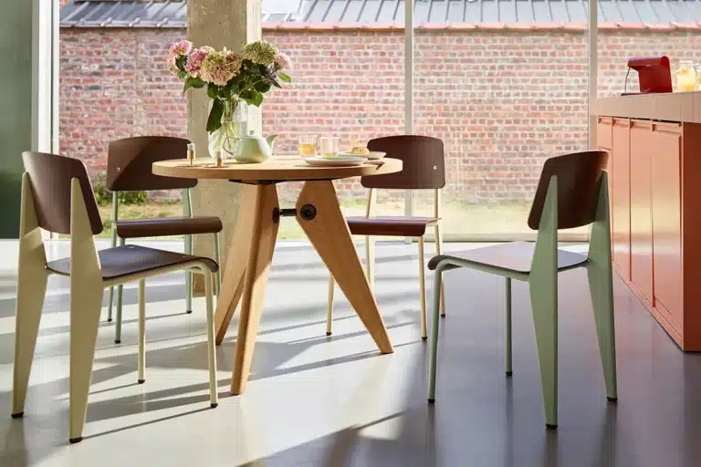 Modern dining room with a round wooden table, four chairs, a vase of flowers, and a brick wall backdrop.