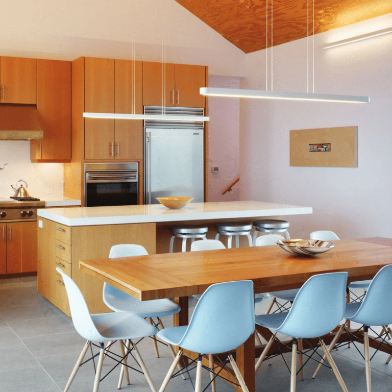 Modern kitchen with wooden cabinets, stainless-steel appliances, a white island, and a wooden dining table with light-blue chairs.